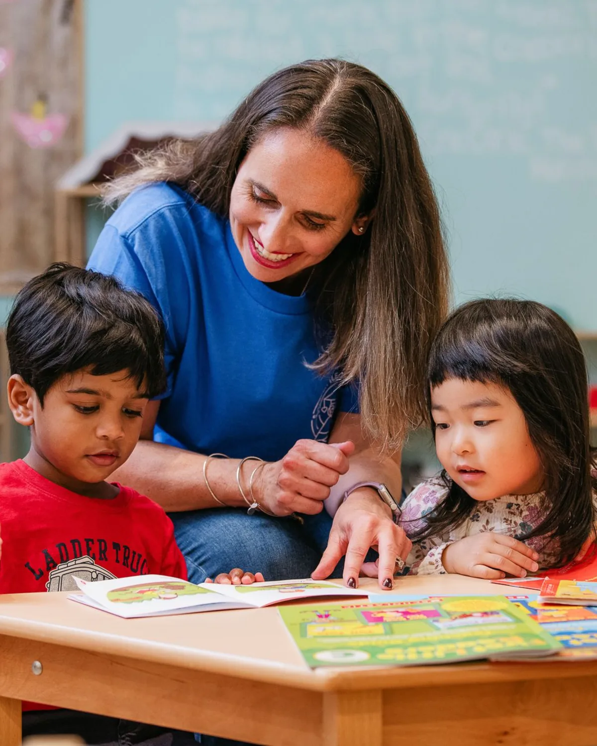 An educator reading a picture book with two young students at The Little Campus